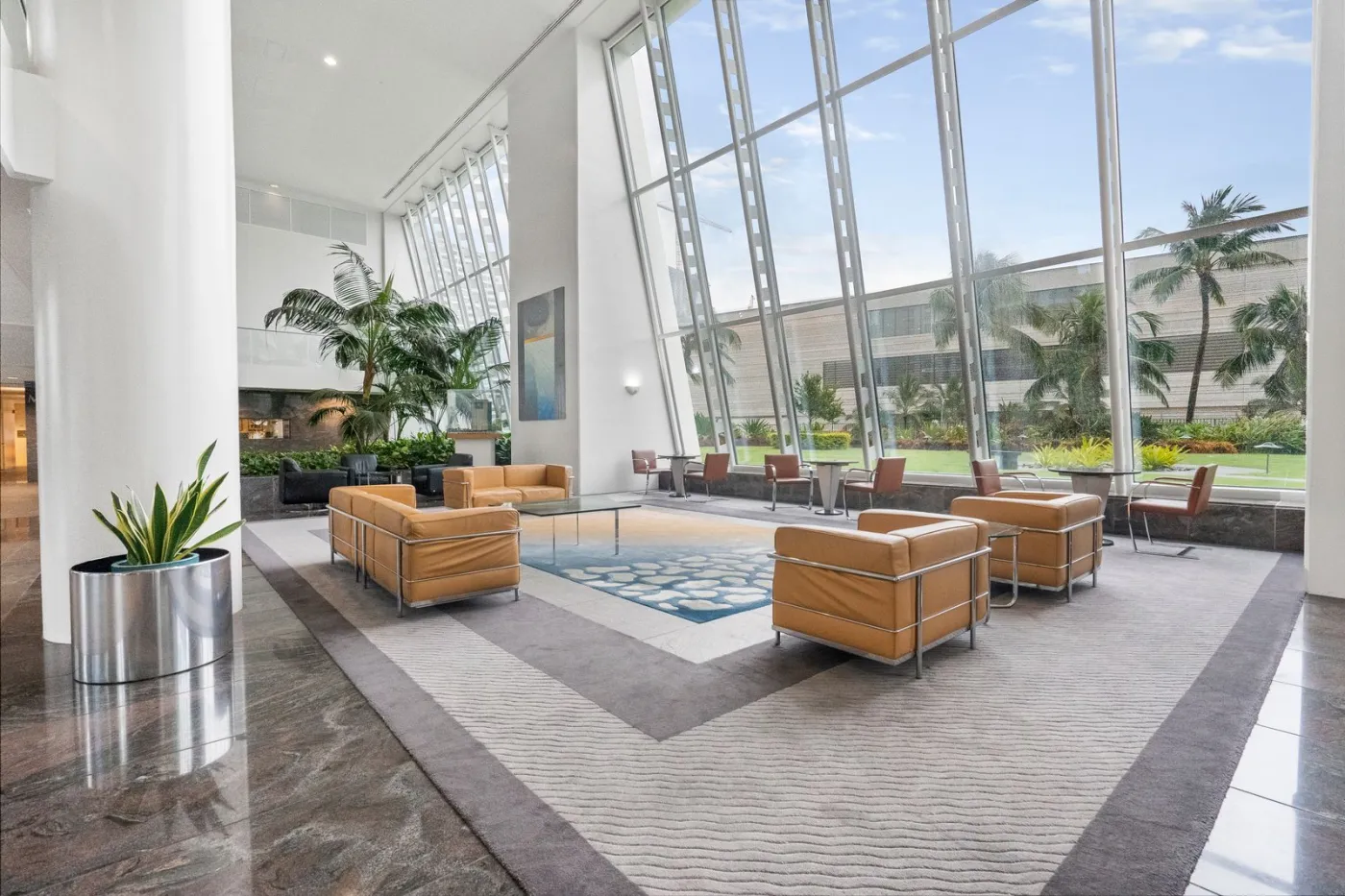 Bright residential building lobby with glass walls, armchairs and indoor plants.